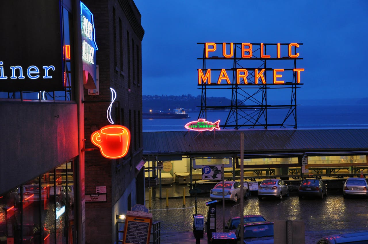 Vibrant nighttime view of Seattles Public Market with neon coffee and market signs illuminated.